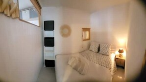 A small, cozy bedroom with a bed, a nightstand, a mirror, and a wall-mounted shelf. - Haven of serenity 100 m from the beach and shops (Le Barcarès)