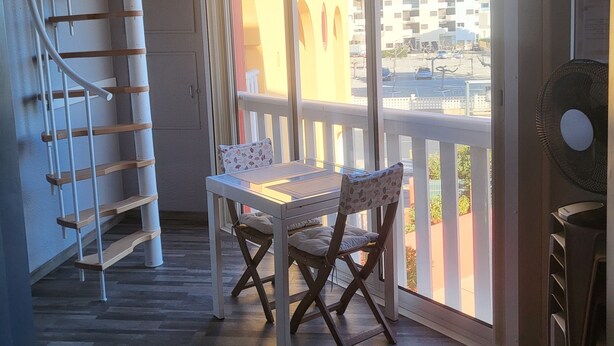 A balcony with a table and chairs, a spiral staircase, and a view of a building. - Residence with swimming pool and sea view - Haven of peace in the heart of the city (Le Barcarès)