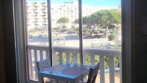 A balcony with a table and chairs, overlooking a parking lot and a building labeled "SYDIA PLAZA". - Residence with swimming pool and sea view - Haven of peace in the heart of the city (Le Barcarès)