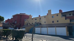 A parking lot with a row of buildings in the background, including a red building and a beige building with a garage. - Residence with swimming pool and sea view - Haven of peace in the heart of the city (Le Barcarès)