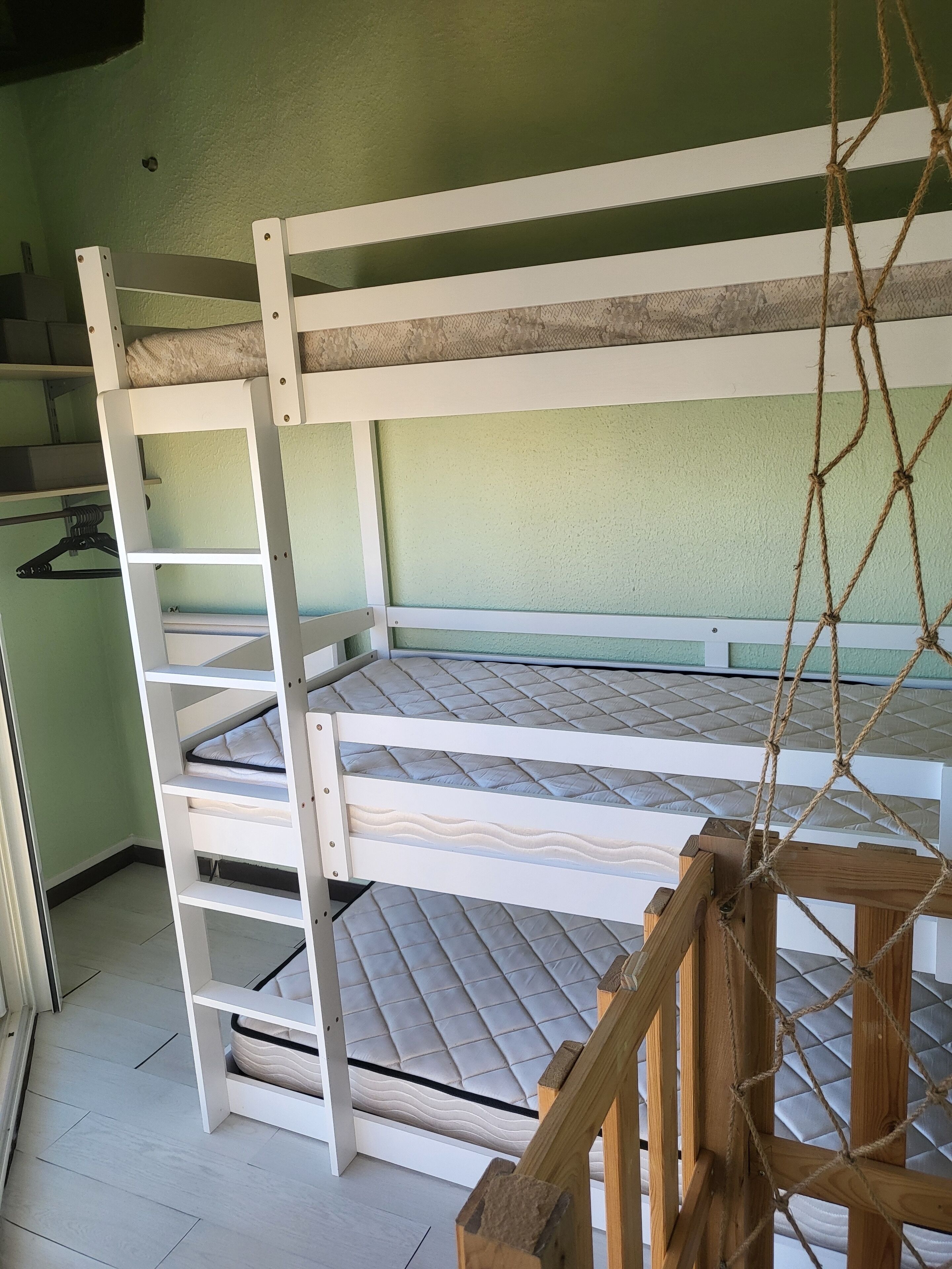 Een stapelbed met een ladder, houten leuningen en een hangtouw.
