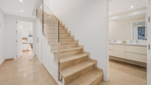 Ein modernes Interieur mit einer Treppe, die zu einem Schlafzimmer führt, einem Badezimmer mit großem Spiegel und einem Flur.