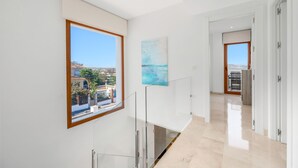 Ein modernes Interieur mit einem großen Fenster, das den Blick auf eine Wohngegend freigibt, einem schlichten Flur und einer Tür, die in einen weiteren Raum führt.