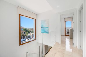 En modern inredning med ett stort fönster som ger utsikt över ett bostadsområde, en minimalistisk hall och en dörr som leder till ett annat rum.