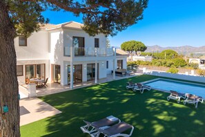 Una casa moderna de dos pisos con piscina, mobiliario exterior y vistas a las montañas.