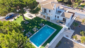 Ein großes, weißes, zweistöckiges Haus mit Swimmingpool, umgeben von einem gepflegten Rasen und Bäumen.