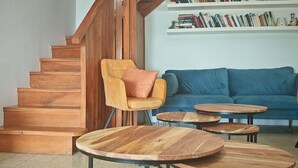 Eine Holztreppe, ein gelber Sessel mit Kissen, ein blaues Sofa und drei Holztische in einem Wohnzimmer.