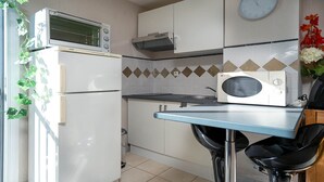 A compact kitchen with a refrigerator, microwave, stove, and a clock on the wall. - Cute little studio for 4 people, parking (Agde)