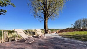 Een verhard buitengebied met twee loungestoelen en een tafel, een boom en uitzicht op het landschap.
