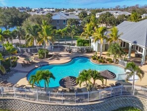 A swimming pool surrounded by palm trees and lounge chairs, with a white fence and a view of houses in the background. - Welcome to your slice of paradise! (Englewood)