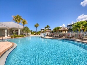 Une piscine d’un bleu éclatant, entourée de palmiers, et un bâtiment à la façade blanche.