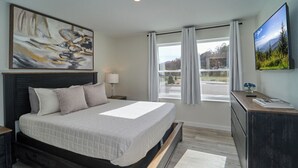 Un dormitorio moderno con una cama grande, un escritorio, un televisor y un cuadro en la pared.