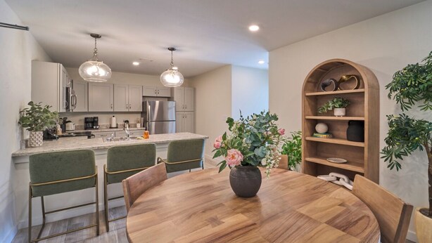 Una cocina moderna con una isla central, sillas tapizadas en verde y una mesa de comedor de madera con un florero.