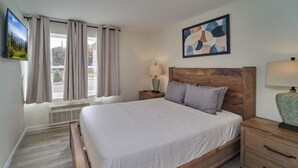 A bedroom with a wooden bed, a nightstand with a lamp, and a window with curtains. - Ruby 102: 1BD | Great LOCATION + Shared Amenities! (Pigeon Forge)