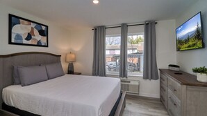 Una camera da letto con un letto, un comodino, una lampada, una cassettiera, una finestra con tende e un quadro appeso al muro.