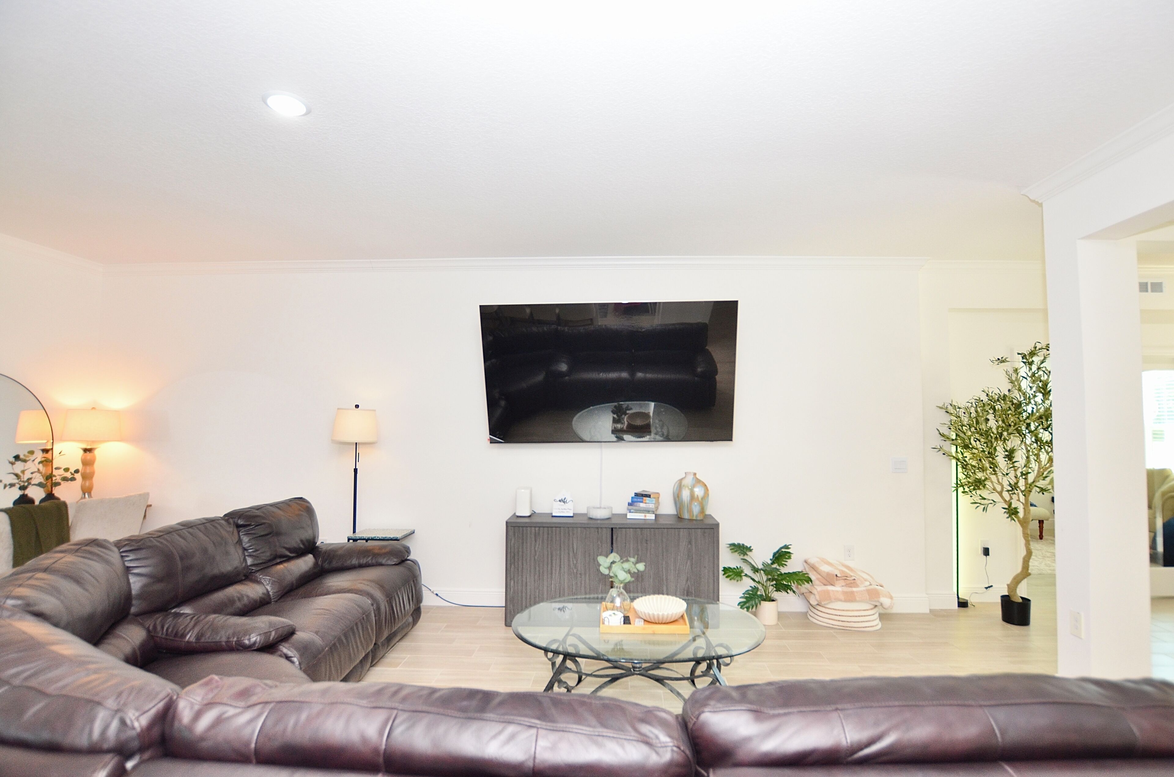 Een moderne woonkamer met een leren bank, een glazen salontafel, een grijze kast en een flatscreen televisie die aan de muur is bevestigd.