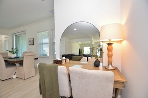 A dining area with a wooden table, beige chairs, a mirror, and a lamp. - The Melshire Place- Brand new 4 bed 3 bath with game room (Port St. Lucie)