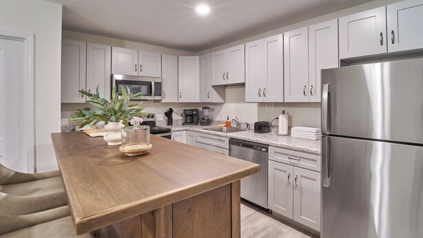 Una cocina moderna con armarios blancos, un refrigerador de acero inoxidable y una isla de madera.