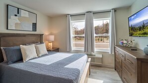 Un dormitorio con una cama grande, una mesita de noche, un aparador, un televisor y una ventana con cortinas.