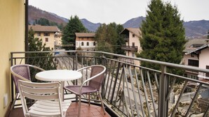 A balcony with two chairs and a small table, overlooking a residential area with houses and a mountain in the background. - Barzio - Garden - Primula (Barzio)