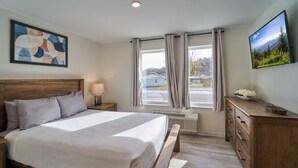 A bedroom with a large bed, a nightstand, a dresser, a TV, and a window with curtains. - Ruby 108: 1BD | Great Location+ Shared Amenities! (Pigeon Forge)