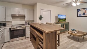 A modern kitchen with white cabinets, stainless steel appliances, a wooden island, and a dining area with a TV and artwork. - Ruby 109: 1BD | Great Location + Shared Amenities! (Pigeon Forge)