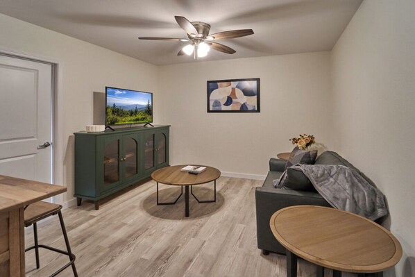 A living room with a wooden floor, a ceiling fan, a television, a cabinet, a sofa, and a coffee table. - Ruby 110: 1BD | Great Location + Shared Amenities! (Pigeon Forge)