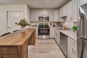 A modern kitchen with white cabinets, stainless steel appliances, a wooden dining table, and a potted plant. - Ruby 112: 1BD | Great Location + Shared Amenities! (Pigeon Forge)