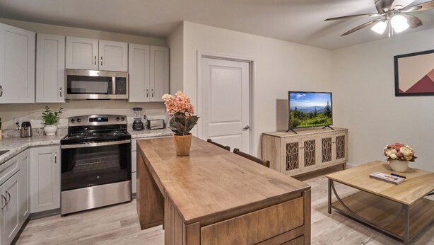 A modern kitchen with stainless steel appliances, a wooden island, and a dining area with a TV and decorative items. - Ruby 113: 1BD | Great Location + Shared Amenities! (Pigeon Forge)