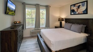 A bedroom with a large bed, a TV on the wall, a dresser, and a window with curtains. - Ruby 113: 1BD | Great Location + Shared Amenities! (Pigeon Forge)