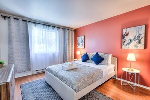 Une chambre à coucher avec un lit, une table de chevet, une lampe et des œuvres d’art accrochées au mur.