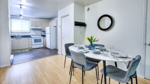 Una cocina compacta con electrodomésticos modernos, una zona de comedor con una mesa redonda y sillas, y un pequeño espejo decorativo en la pared.