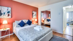 Una habitación de hotel con cama, lámparas de noche, un espejo y obras de arte en las paredes.