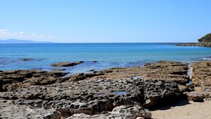 Uma costa rochosa com águas azul-claras e montanhas ao longe.