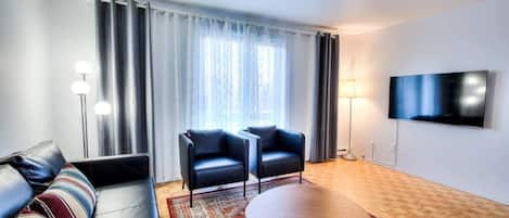 Un salon moderne comprenant un canapé, deux fauteuils, une table basse, un téléviseur et un tapis à motifs.