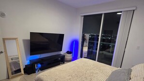 A bedroom with a large bed, a flat-screen TV, a sliding glass door to a balcony, and a city view at night. - Luxury penthouse 1-bedroom By Miami river amazing view, parking, Gym & Pool (Miami)