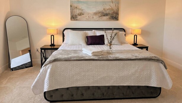 A neatly made bed with a quilted headboard, two bedside lamps, a mirror, and a painting above the bed. - Updated Family Retreat in Gated Resort Community - Pool, Gym, Near Parks & MCO (Kissimmee)