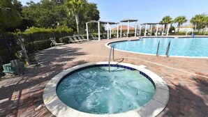 A hot tub surrounded by a brick patio, with a pool and lounge chairs in the background. - Updated Family Retreat in Gated Resort Community - Pool, Gym, Near Parks & MCO (Kissimmee)