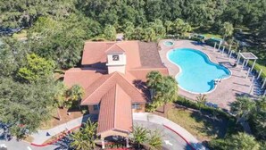 An aerial view of a property with a swimming pool, a covered patio area, and a building with a clock tower. - Updated Family Retreat in Gated Resort Community - Pool, Gym, Near Parks & MCO (Kissimmee)