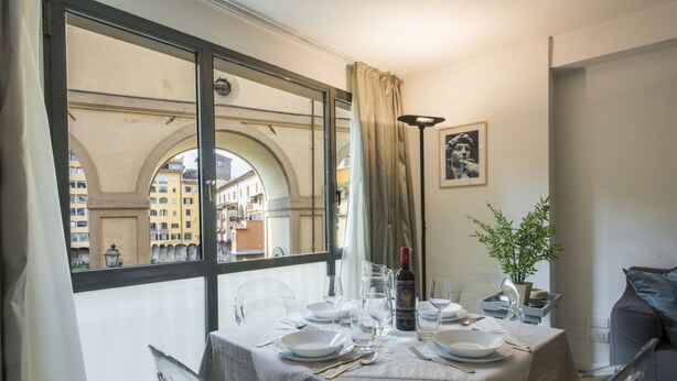 Comedor con mesa preparada para dos personas, una botella de vino y una planta en maceta.