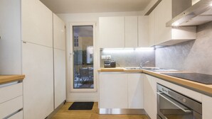 Una cocina compacta con armarios blancos, encimera de madera, horno integrado y ventana con vistas a un patio.