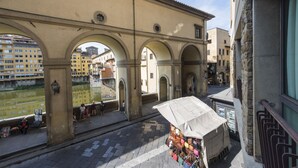 Una calle con un arco, un quiosco que vende bolsos y un edificio con tejado de tejas.