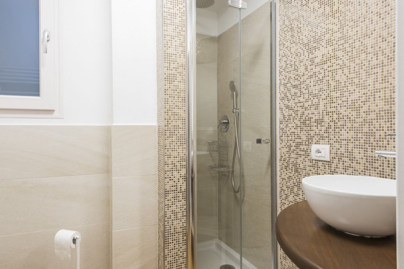 A bathroom with a glass shower enclosure, a white sink, and tiled walls.