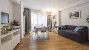 Una sala de estar moderna con comedor, piso de madera, un sofá gris y un televisor de pantalla plana montado en la pared.