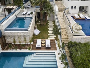Un espace piscine moderne doté de plusieurs piscines, de chaises longues et d’un jardin bien entretenu.