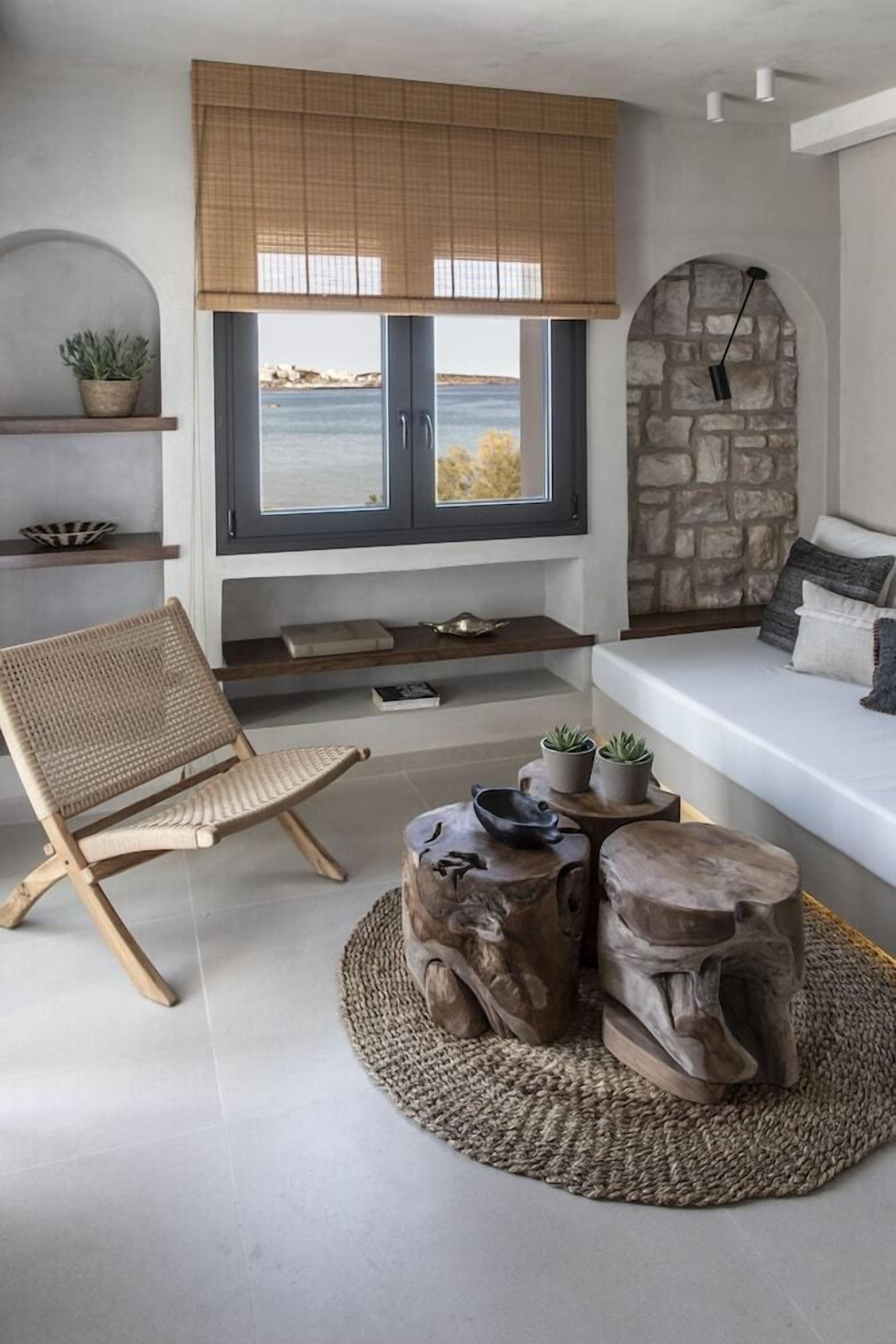 Una sala de estar moderna con vista al mar, una pared de piedra y un área de descanso con sofá y sillón.