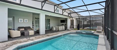 Una piscina interior con un patio cubierto, sillas de descanso y un televisor.