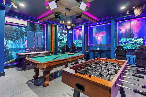 Una habitación con mesa de billar, mesa de futbolín y dos grandes acuarios.