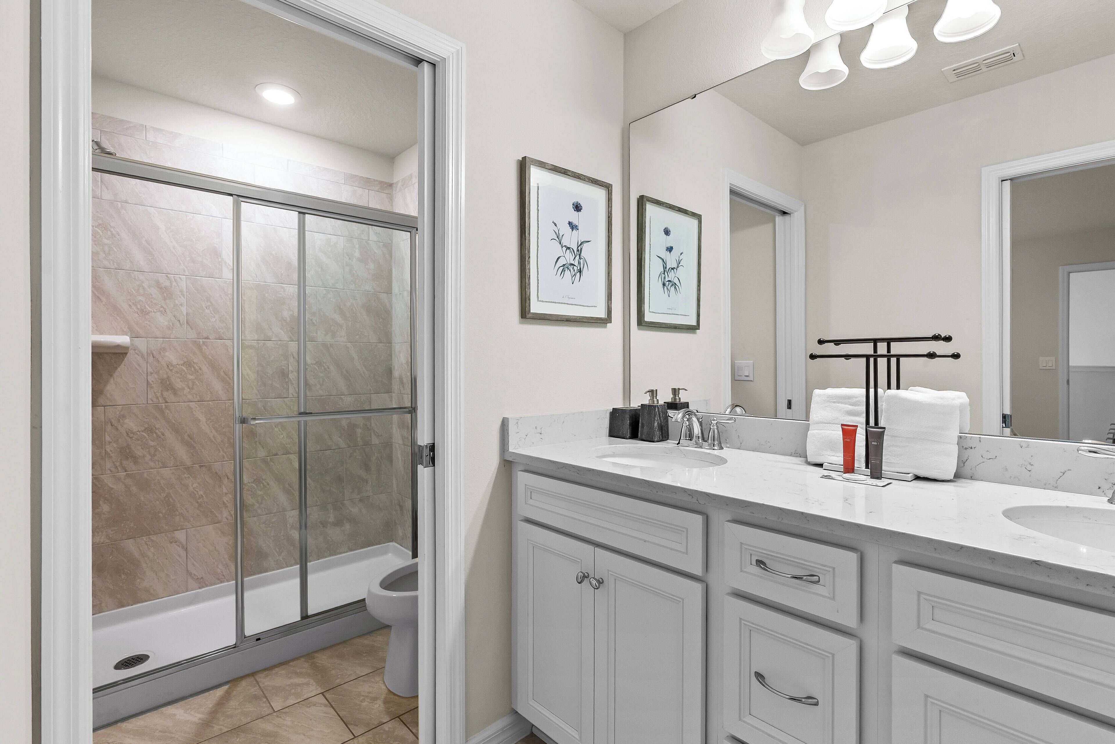 A modern bathroom with a glass shower enclosure, a white vanity with a sink, and framed artwork on the wall.