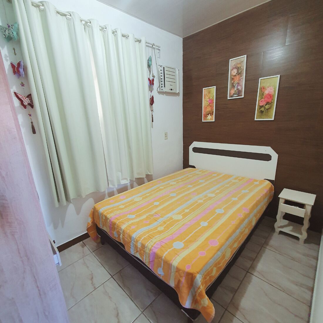 A bedroom with a bed, curtains, a wall-mounted air conditioner, and three framed pictures.